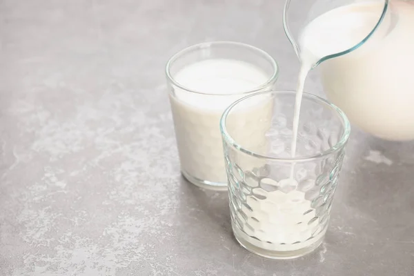 Pouring of milk from jug into glass on table. Fresh dairy product — Stock Photo, Image