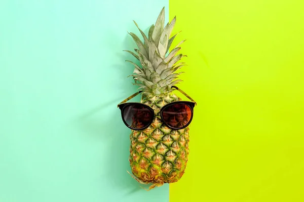 Ananas frais mûr avec des lunettes de soleil sur fond de couleur, vue de dessus — Photo