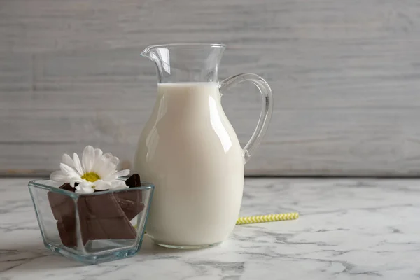 Jug with milk and chocolate pieces on table — Stock Photo, Image