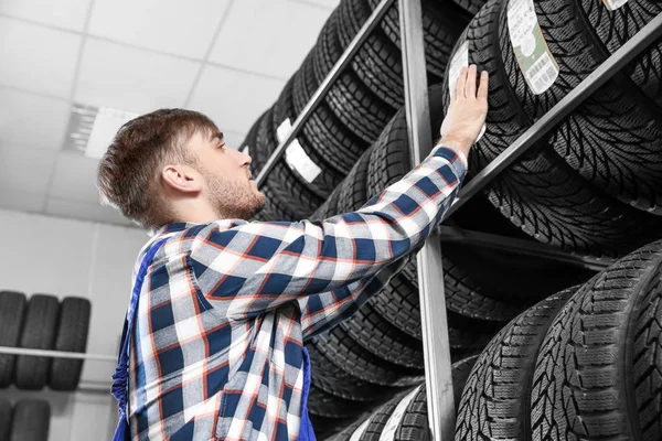 Jovem mecânico masculino com pneus de carro no centro de serviços de automóveis — Fotografia de Stock