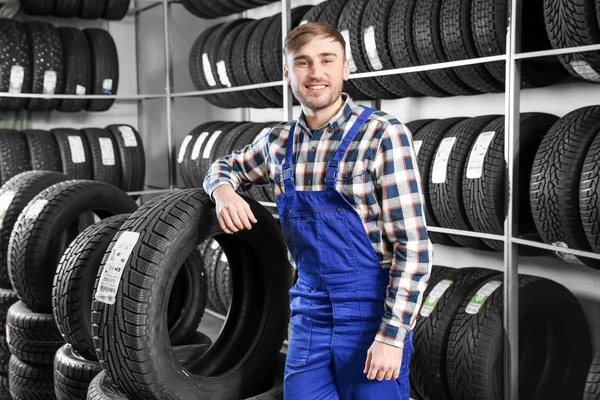 Jovem mecânico masculino com pneus de carro no centro de serviços de automóveis — Fotografia de Stock