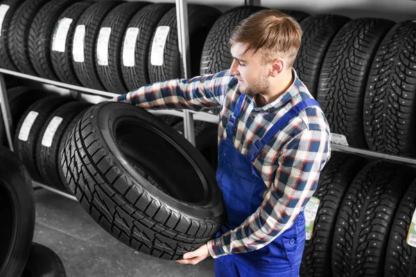 Jovem mecânico masculino com pneu de carro no centro de serviços de automóveis — Fotografia de Stock