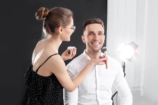 Profesionální make-up umělec, který pracuje s mladým mužem v ateliéru — Stock fotografie