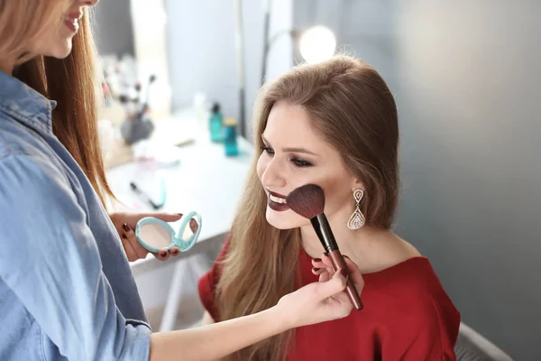 Profesionální make-up umělec, který pracuje s krásnou mladou ženou ve studiu — Stock fotografie