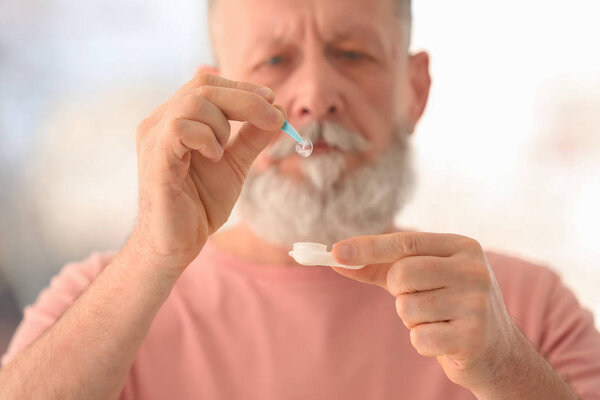 Senior man taking contact lens from container on blurred background