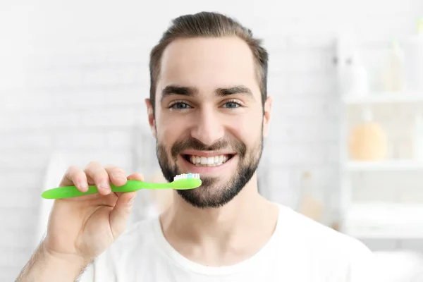 Young man brushing his teeth indoors — Stock Photo, Image