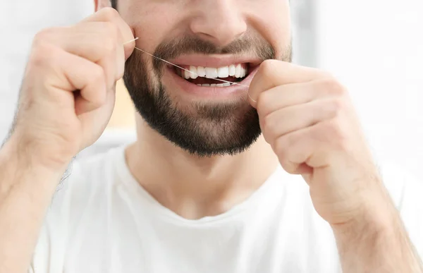 Young man flossing his teeth indoors — Stock Photo, Image