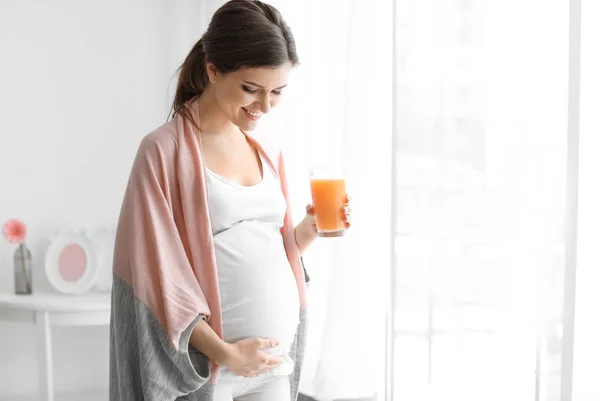 Молодая беременная женщина держит стакан с соком дома — стоковое фото