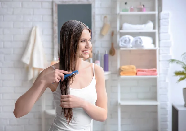 Молодая женщина расчесывает волосы после нанесения маски в ванной комнате — стоковое фото