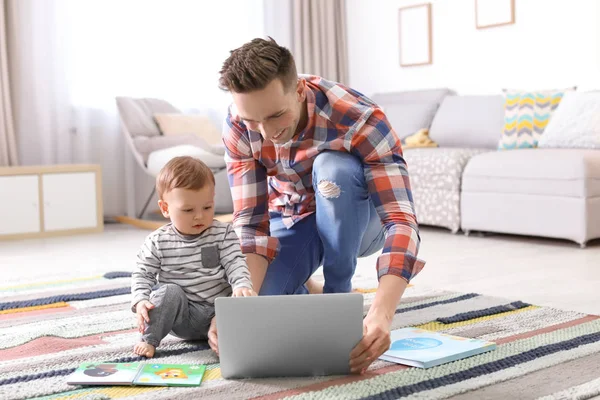 Молодий батько зі своїм милим маленьким сином використовує ноутбук вдома — стокове фото