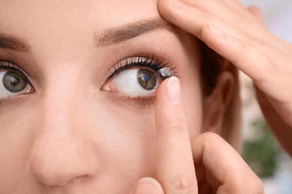 Young woman putting contact lens in her eye, closeup
