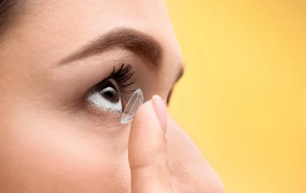 Jovem mulher colocando lente de contato em seu olho no fundo de cor, close-up — Fotografia de Stock