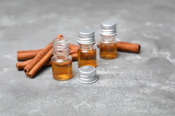 Bottles with cinnamon oil and sticks on grey background