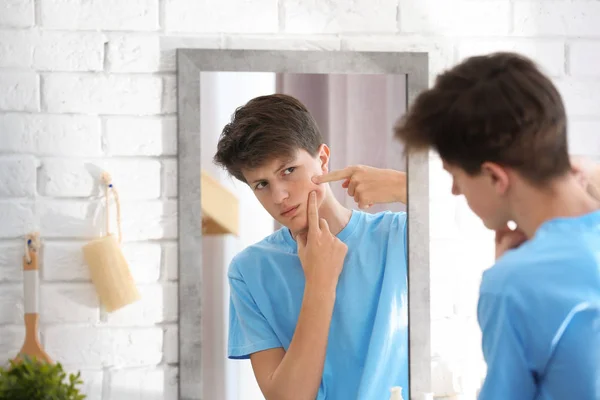 Хлопчик-підліток з проблемою акне дивиться в дзеркало вдома — стокове фото