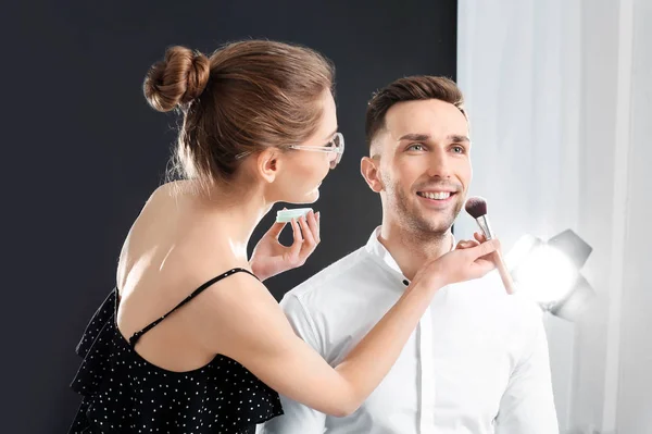 Profesionální make-up umělec, který pracuje s mladým mužem v ateliéru — Stock fotografie