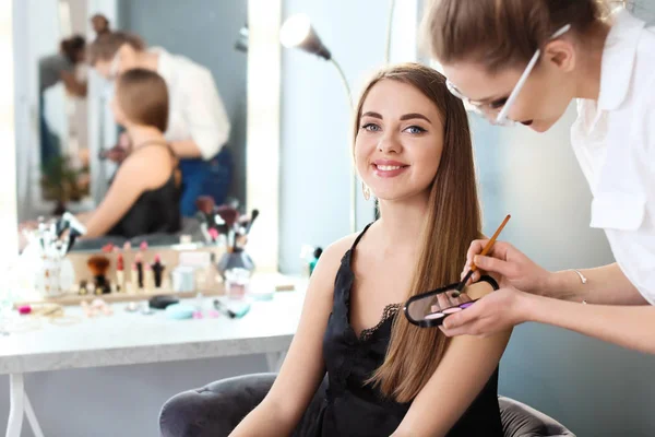 Professionell makeupartist arbetar med vacker ung kvinna i studio — Stockfoto