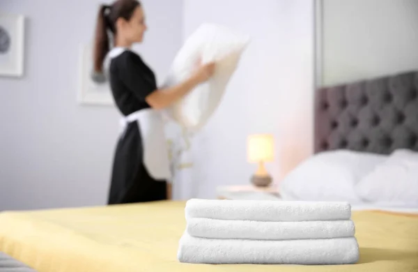 Pilha de toalhas e empregada desfocada no fundo no quarto de hotel — Fotografia de Stock