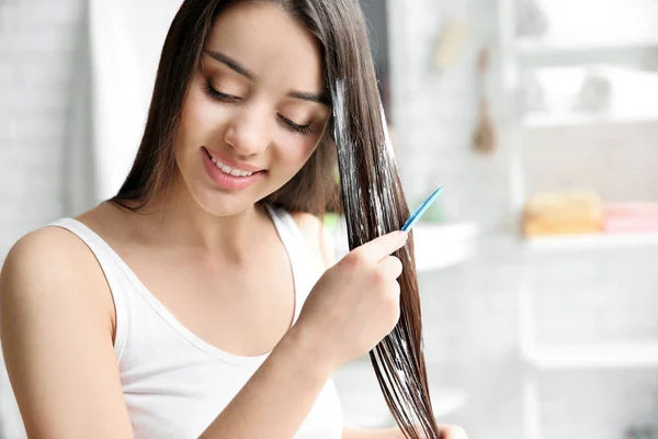 Молодая женщина расчесывает волосы после нанесения маски в ванной комнате — стоковое фото