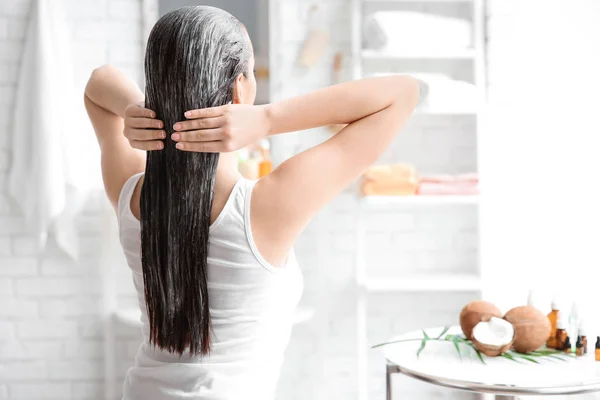 Mujer joven aplicando aceite sobre el cabello en el baño —  Fotos de Stock