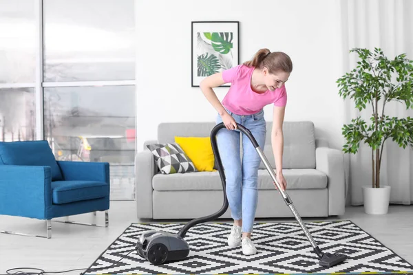 Young woman hoovering carpet at home — Stock Photo, Image