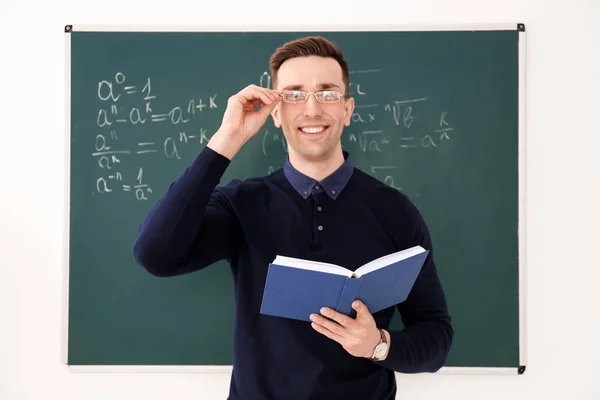 Guru laki-laki muda dengan buku berdiri di kelas — Stok Foto