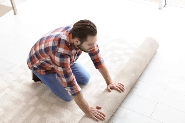 Hombre rodando nuevo suelo de alfombra en la habitación — Foto de Stock