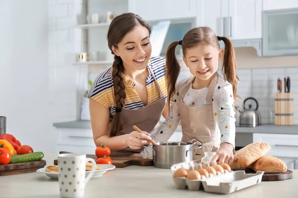 Молодая няня с милой маленькой девочкой готовит вместе на кухне — стоковое фото