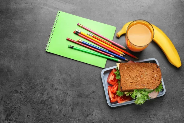 Composición plana con sabroso sándwich, vaso de jugo y papelería sobre fondo gris — Foto de Stock