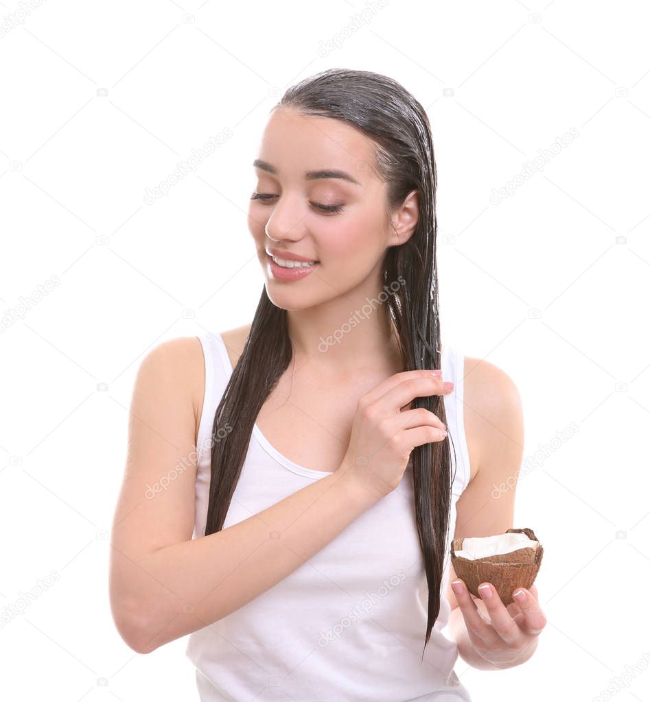 Young woman applying coconut oil onto hair against white background