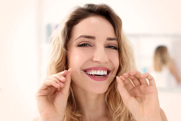 Mujer joven usando hilo dental en el interior —  Fotos de Stock