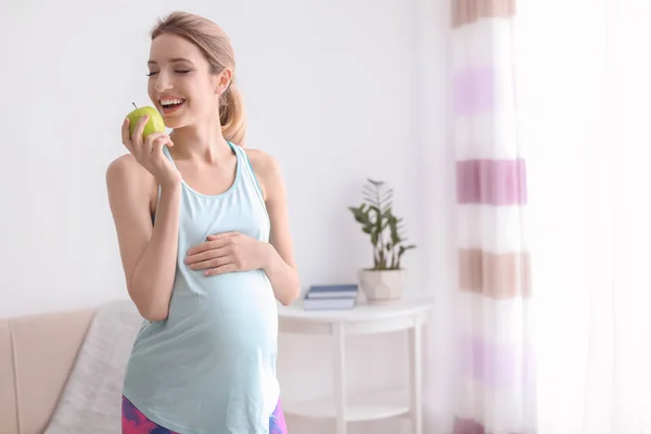 Молода вагітна жінка їсть яблуко вдома — стокове фото