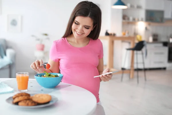 Jovem grávida comendo salada de legumes à mesa na cozinha — Fotografia de Stock