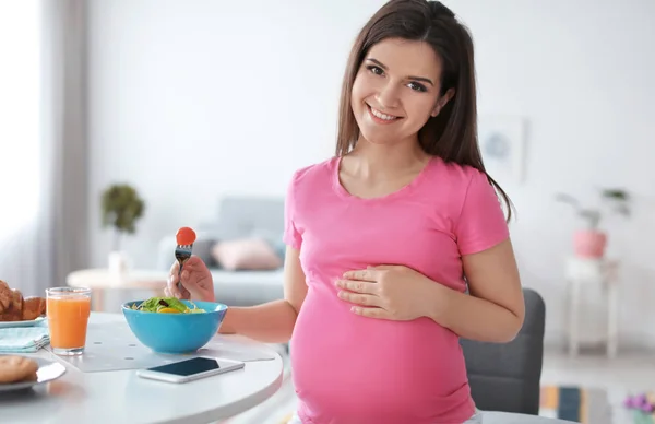 Jovem grávida comendo salada de legumes à mesa na cozinha — Fotografia de Stock