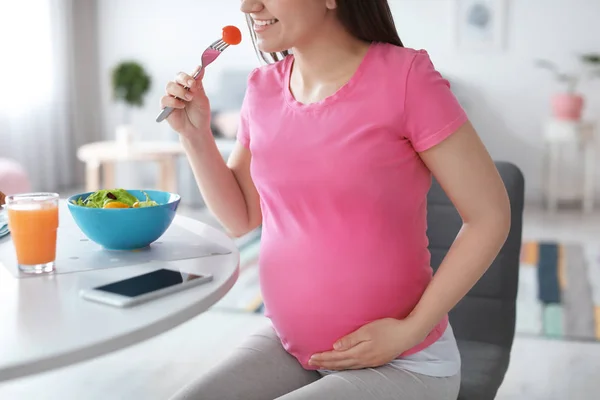 Young pregnant woman eating vegetable salad at table in kitchen — Stock Photo, Image