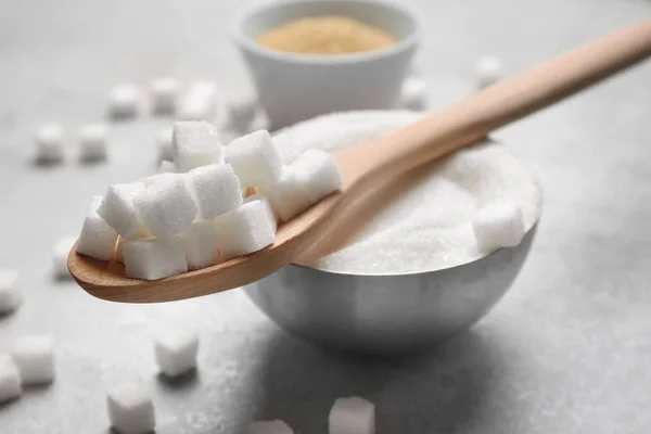 Cucchiaio e ciotola con zucchero bianco su sfondo grigio — Foto Stock