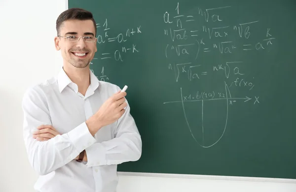 Junger männlicher Lehrer mit Kreide in der Nähe der Tafel im Klassenzimmer — Stockfoto