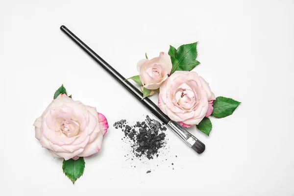 Flat lay composition with makeup brush and flowers on white background