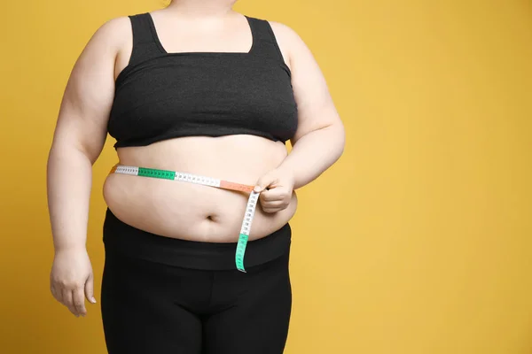 Mulher com excesso de peso com fita métrica no fundo de cor — Fotografia de Stock
