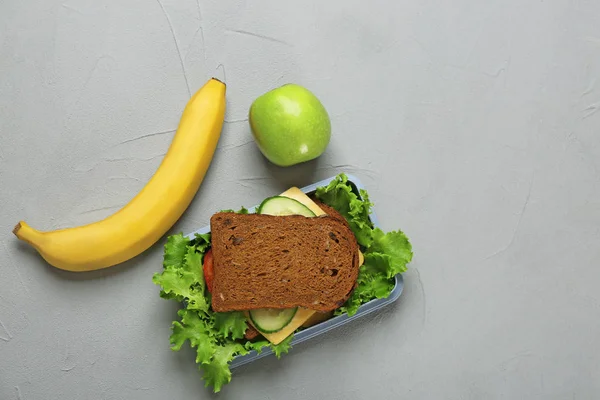 Matlåda med god smörgås och frukt på grå bakgrund, ovanifrån — Stockfoto