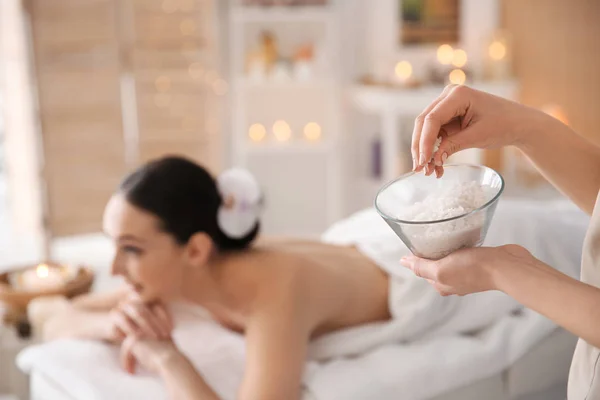 Cosmetologist holding bowl with body scrub in spa salon