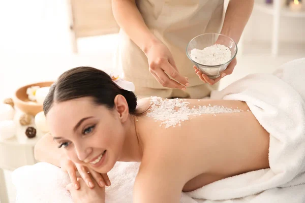 Hermosa mujer joven teniendo masaje con exfoliante corporal en el salón de spa —  Fotos de Stock