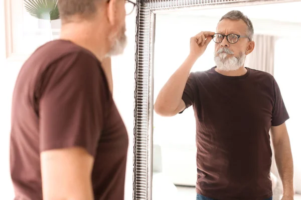 Зрелый мужчина смотрит в зеркало дома — стоковое фото