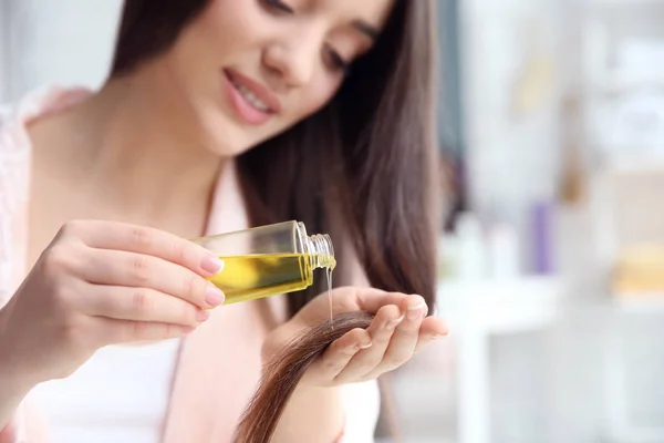 Young woman applying oil onto hair at home — Stock Photo, Image
