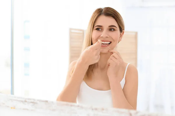 Ung kvinna tandtråd tänderna i badrum — Stockfoto
