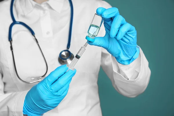 Arzt mit Spritze und Medikamenten zur Impfung auf farbigem Hintergrund — Stockfoto