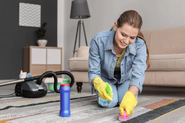 Ung kvinna rengöring mattan hemma — Stockfoto