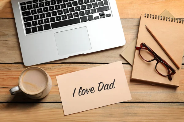 Karta s frází "I love táta" poblíž laptop a šálek kávy na dřevěný stůl, pohled shora. Oslava Den otců — Stock fotografie