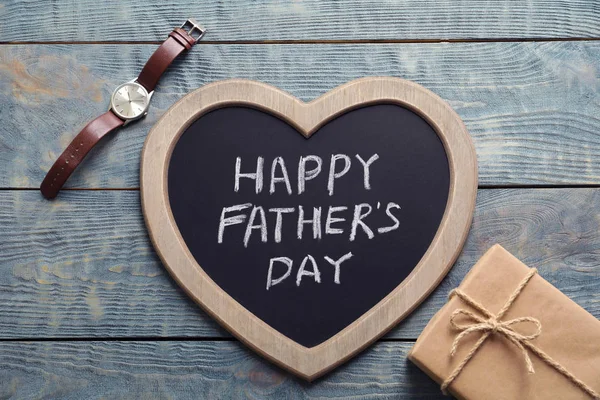 Gift box, watch and chalkboard with words HAPPY FATHER\'S DAY on wooden background, top view
