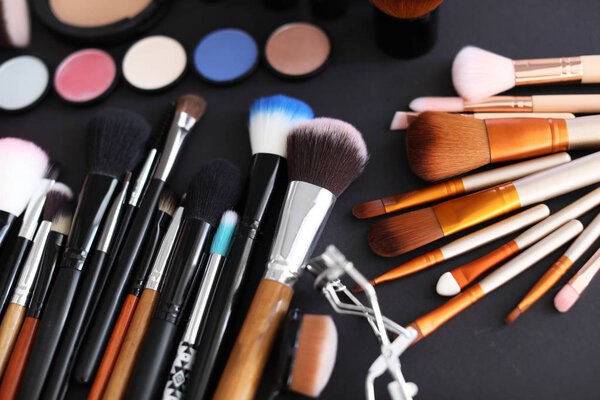 Different makeup brushes and cosmetic products on black background