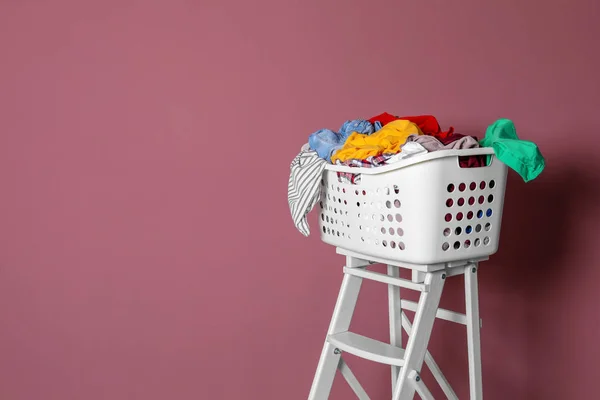 Laundry basket with dirty clothes on step ladder against color background — Stock Photo, Image
